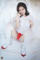 A woman in a white and red outfit is sitting on a bed.