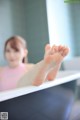 A woman in a pink tank top is sitting in a bathtub with her feet up.