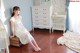 A woman in a white dress sitting on a wooden floor.