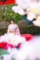 A woman in a pink kimono sitting under a red umbrella.