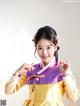 A woman in a yellow and purple hanbok poses for a picture.