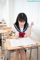 A woman sitting at a desk writing in a classroom.