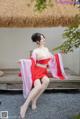 A woman in a red kimono sitting on a wooden bench.