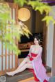 A woman in a pink and red kimono sitting on a wooden bench.