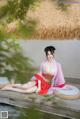 A woman in a red and pink kimono sitting on a wooden bench.