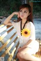 A woman sitting on a wooden bench with a sunflower in her hand.