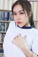 A woman in a white shirt is posing in front of a bookshelf.