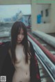 A naked asian woman standing on a train track.