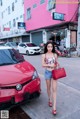 A woman walking down the street in front of a red car.