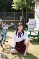 A woman in a school uniform sitting on the ground next to a bike.