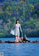 A woman in a white dress standing on a rock in the water.